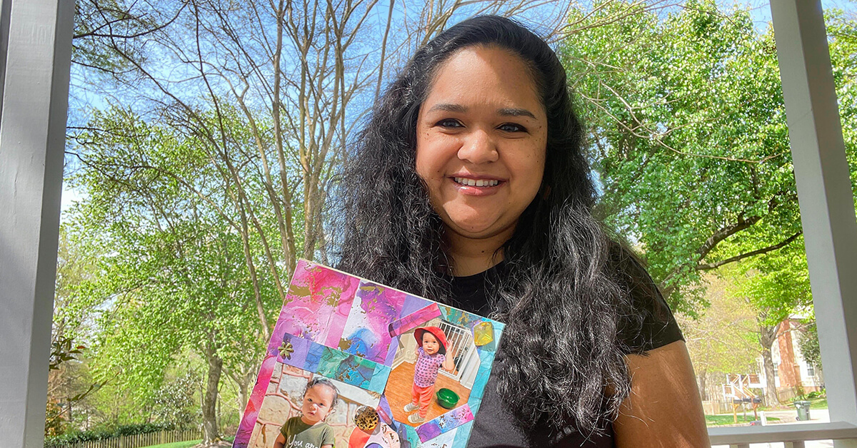 Capital One associate stands outside under trees holding her piece of artwork, a colorful collage with images of her children.